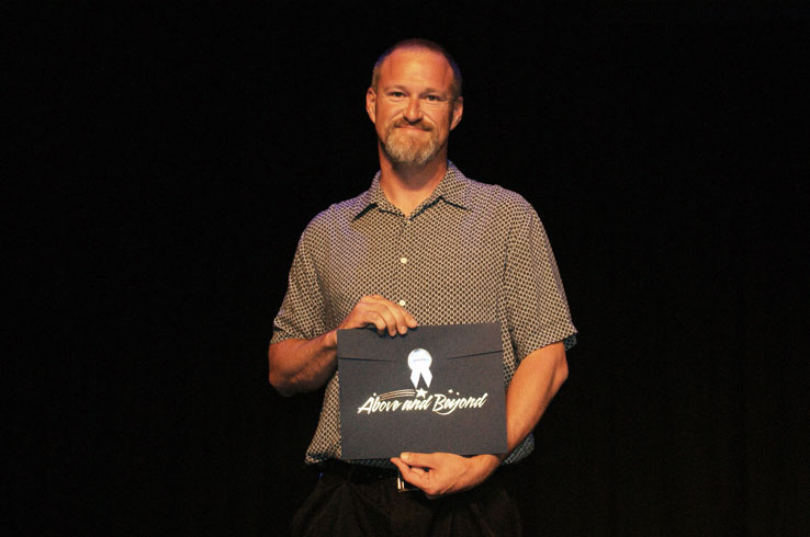 A man holding an award that says Above and Beyond